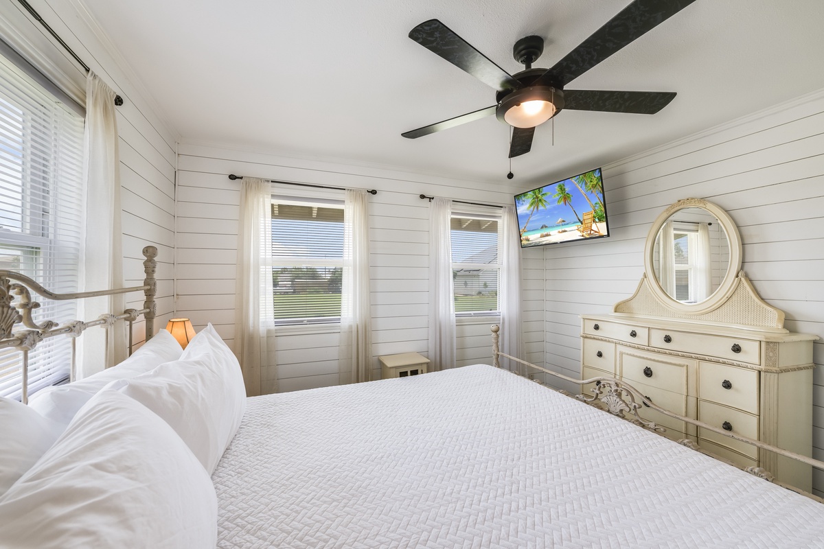 Unwind in your bright, airy bedroom with coastal cottage charm. Crisp white linens and shiplap walls create a serene retreat where restful nights await beneath the gentle ceiling fan.
