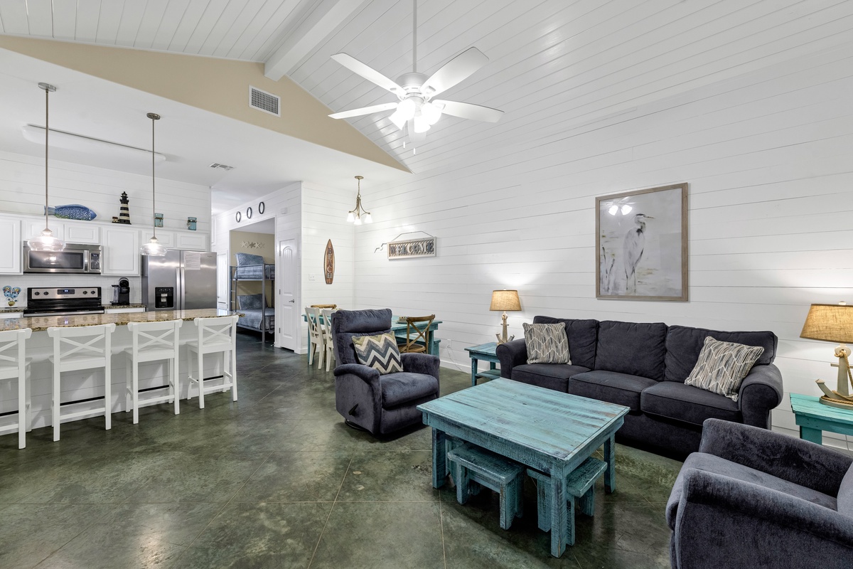 Unwind in your spacious open-concept living area with coastal charm, featuring comfortable seating and a fully equipped kitchen for memorable gatherings.