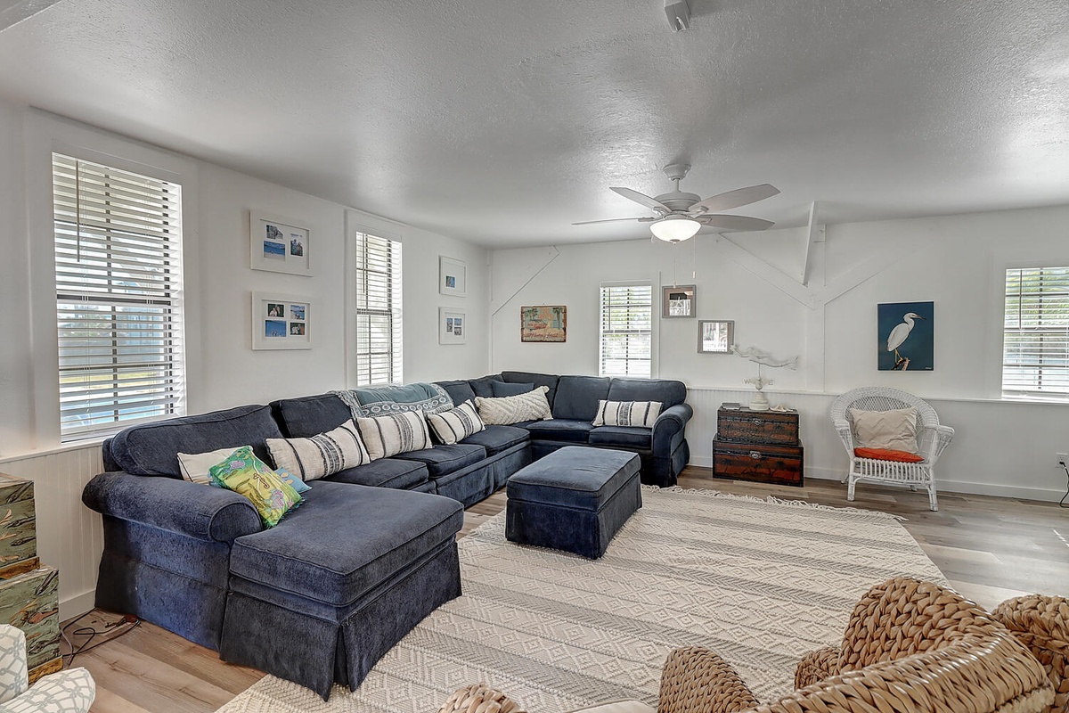 Relax in your spacious living room with plush sectional seating, coastal artwork, and ceiling fan comfort for the perfect gathering spot.
