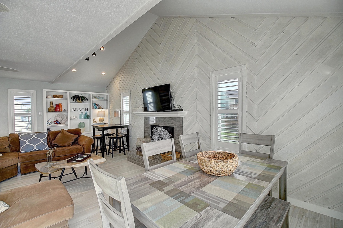 Cozy up in this bright open living space where coastal charm meets modern comfort. Your dining table awaits family meals while the fireplace sets the mood.