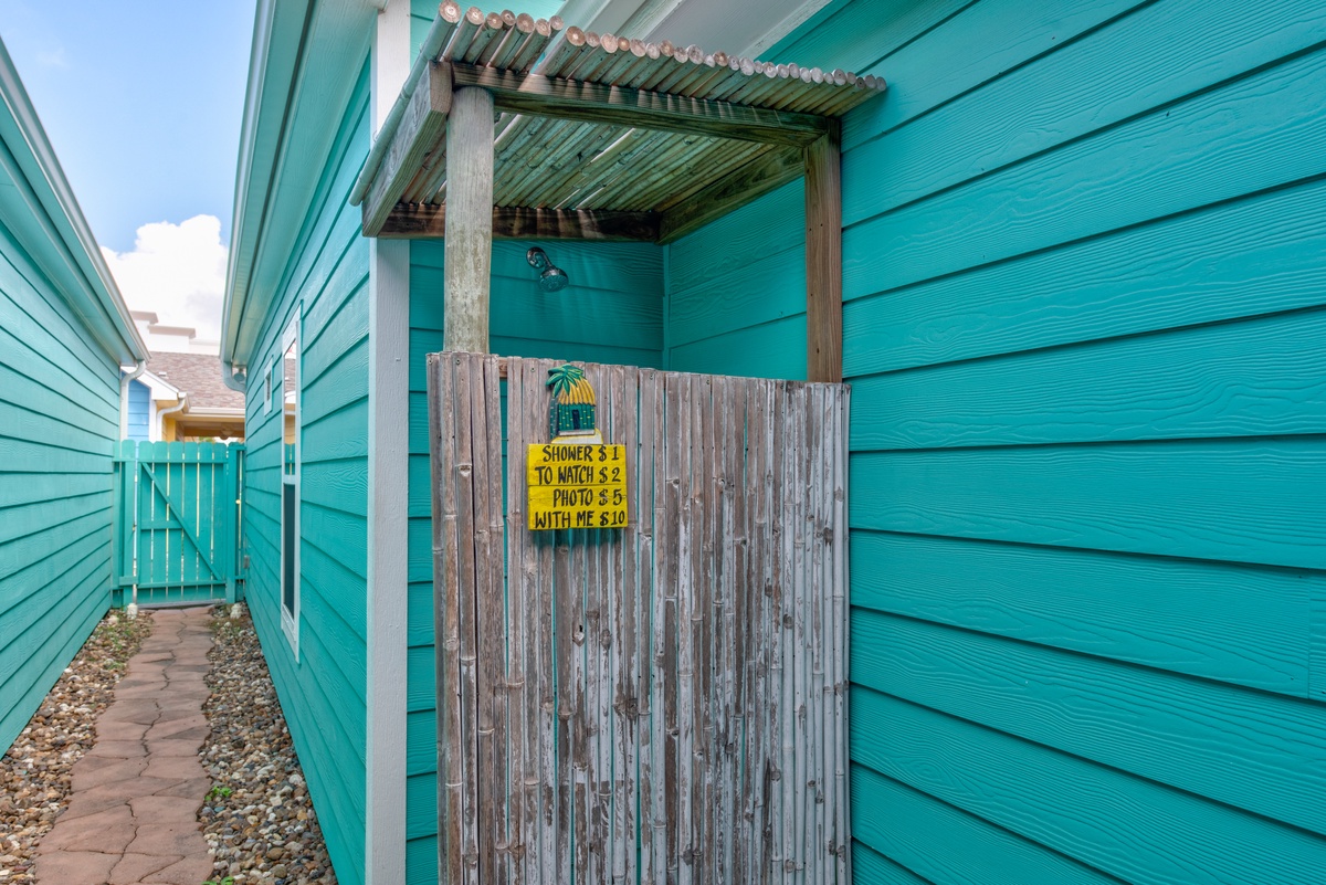 Bright turquoise beach house entrance with charming outdoor shower area and coastal pathway leading to your seaside retreat.