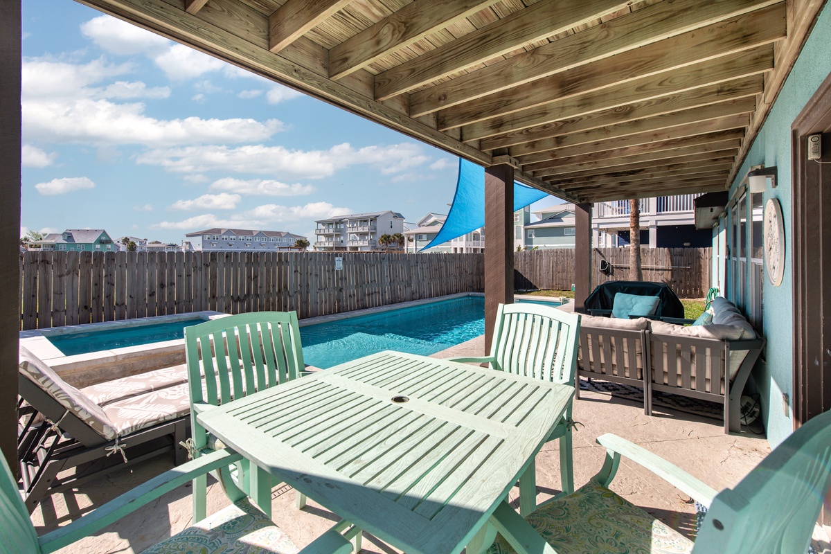 Your covered patio offers poolside dining with turquoise furniture and BBQ, perfect for leisurely meals in coastal comfort.