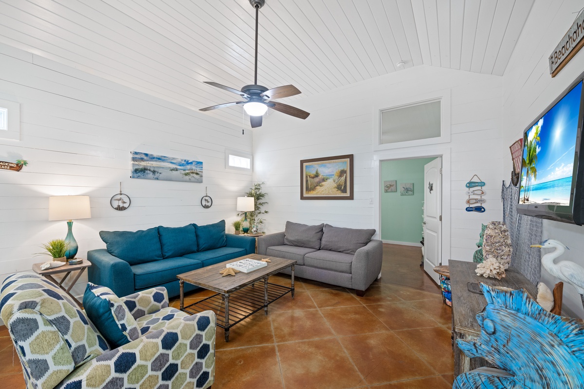 Sink into plush sofas under soaring ceilings while ocean breezes from your ceiling fan create the perfect coastal retreat atmosphere.