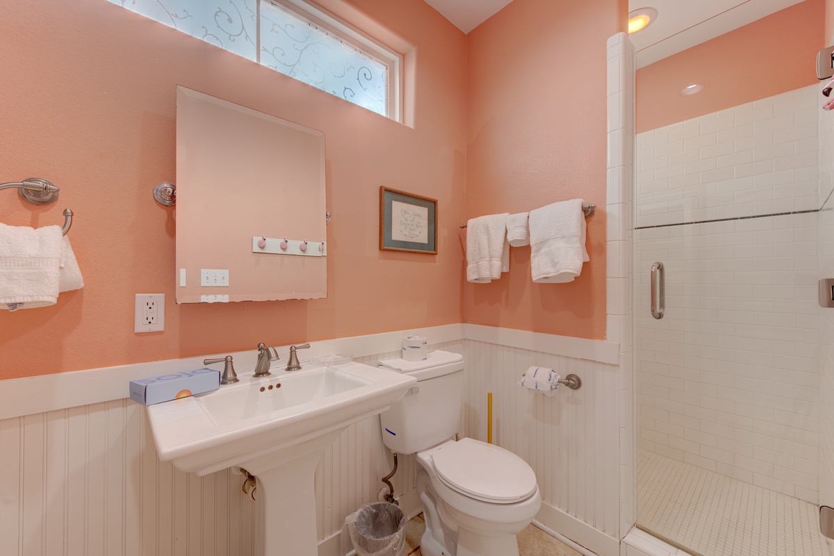 Step into your bright, cheerfully appointed bathroom with warm coral walls, pristine white fixtures, and a spacious walk-in shower ready for your refreshing start.