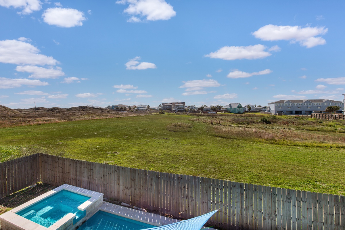 Second floor balcony overlooks the pool, hot tub, and expansive coastal landscape under bright blue skies.