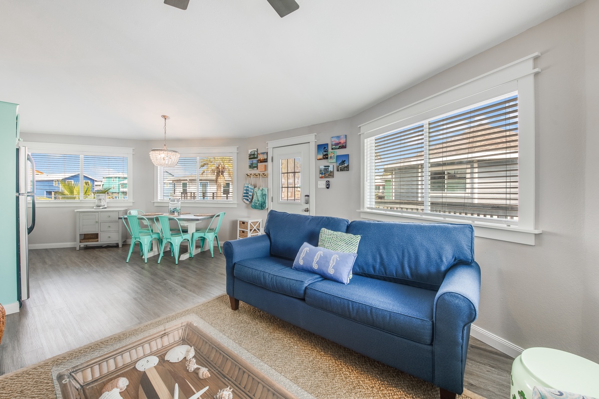 Your bright, beach-themed living space flows seamlessly into the dining area, where turquoise chairs invite relaxed meals while palm trees sway outside your windows.