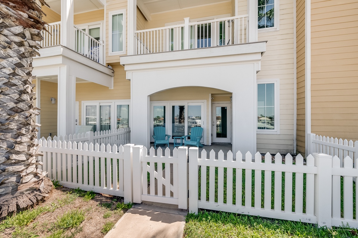 Charming coastal property with private patio featuring turquoise chairs behind white picket fence.