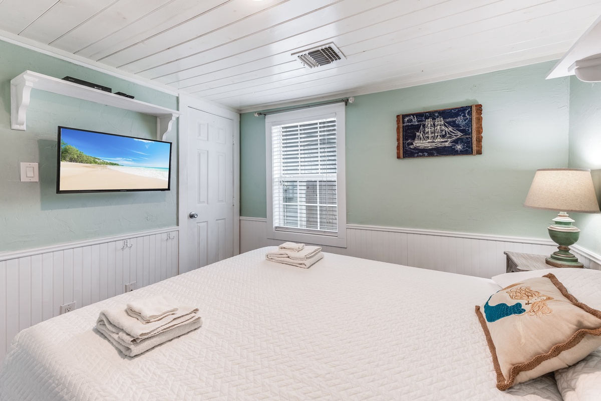 Drift off peacefully in your coastal-themed bedroom with soothing sea-green walls, fresh white linens, and a wall-mounted TV for evening relaxation.