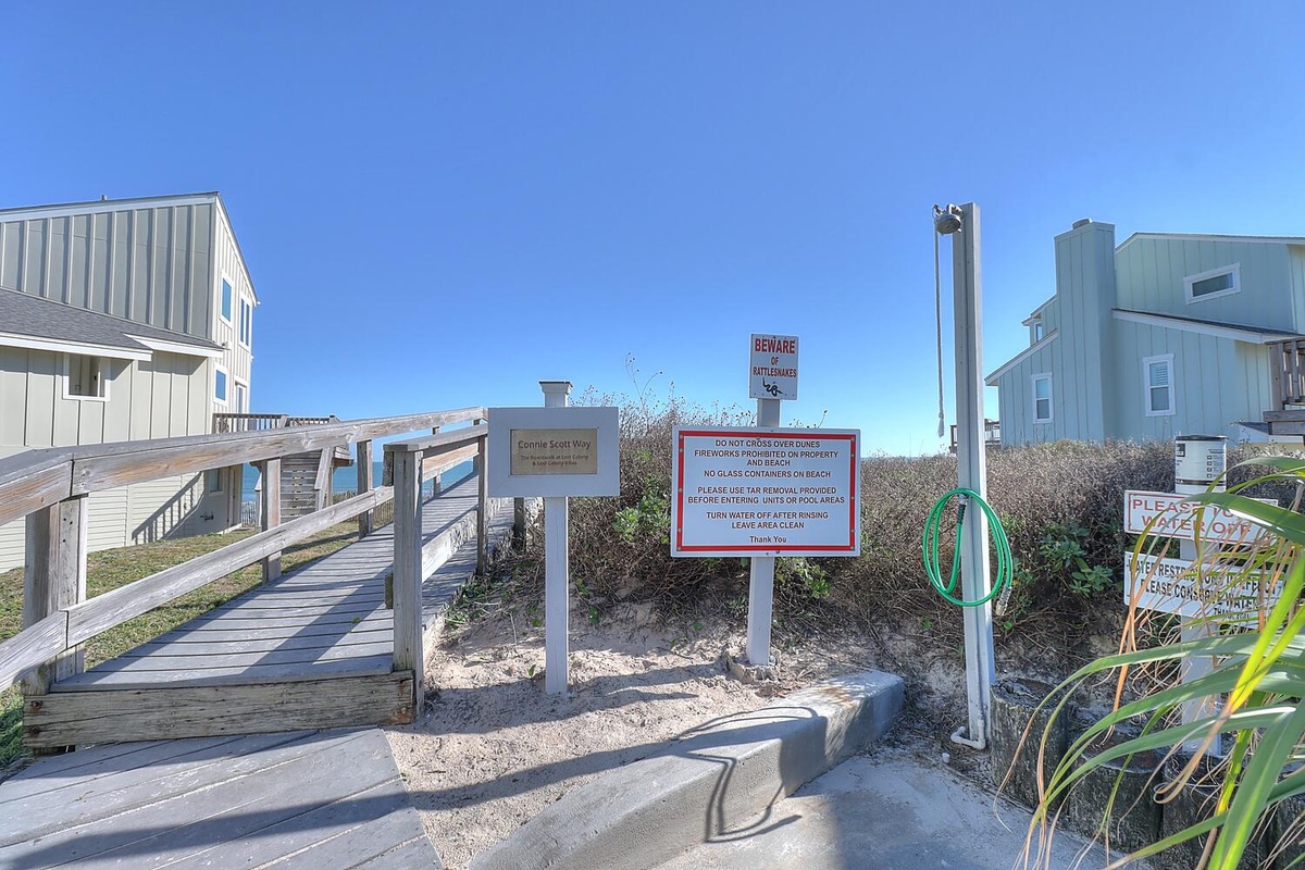 The property's beach access walkway leads through a quiet coastal neighborhood under clear blue skies, with posted guidelines ensuring a pleasant experience for all guests.
