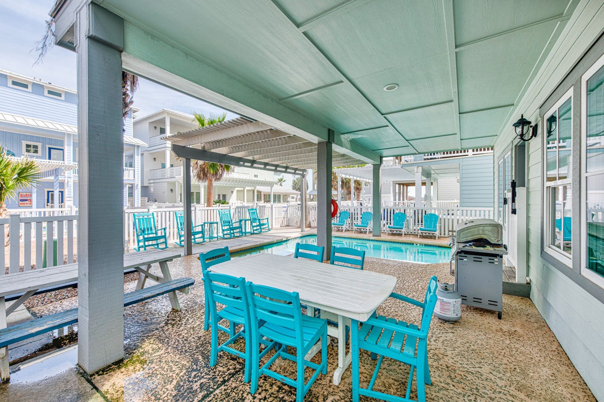 Your covered poolside dining area features bright turquoise chairs and table, perfect for meals while staying cool under the shade.