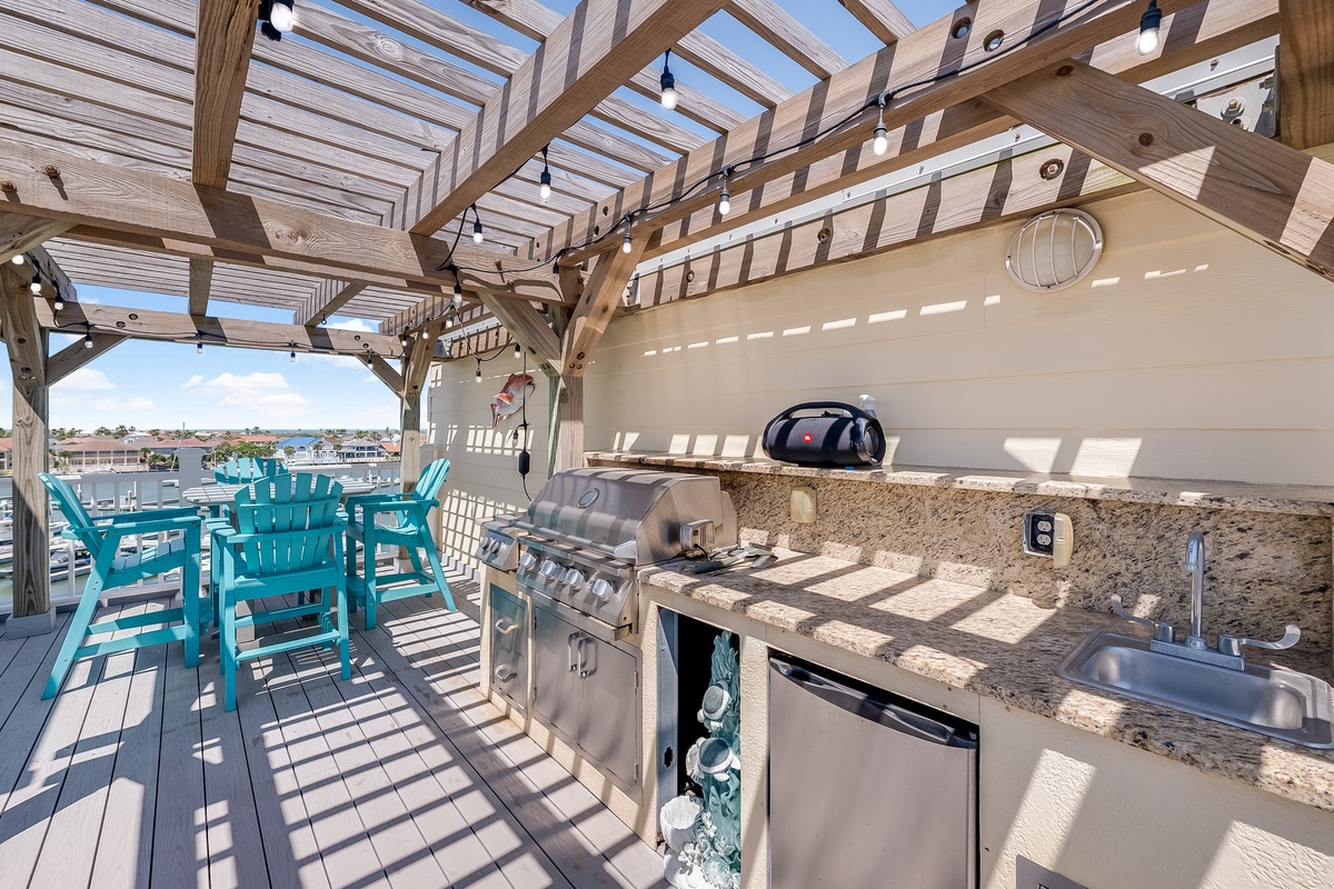 Your rooftop deck features a full outdoor kitchen with granite counters, BBQ grill, and dining chairs under pergola shade.