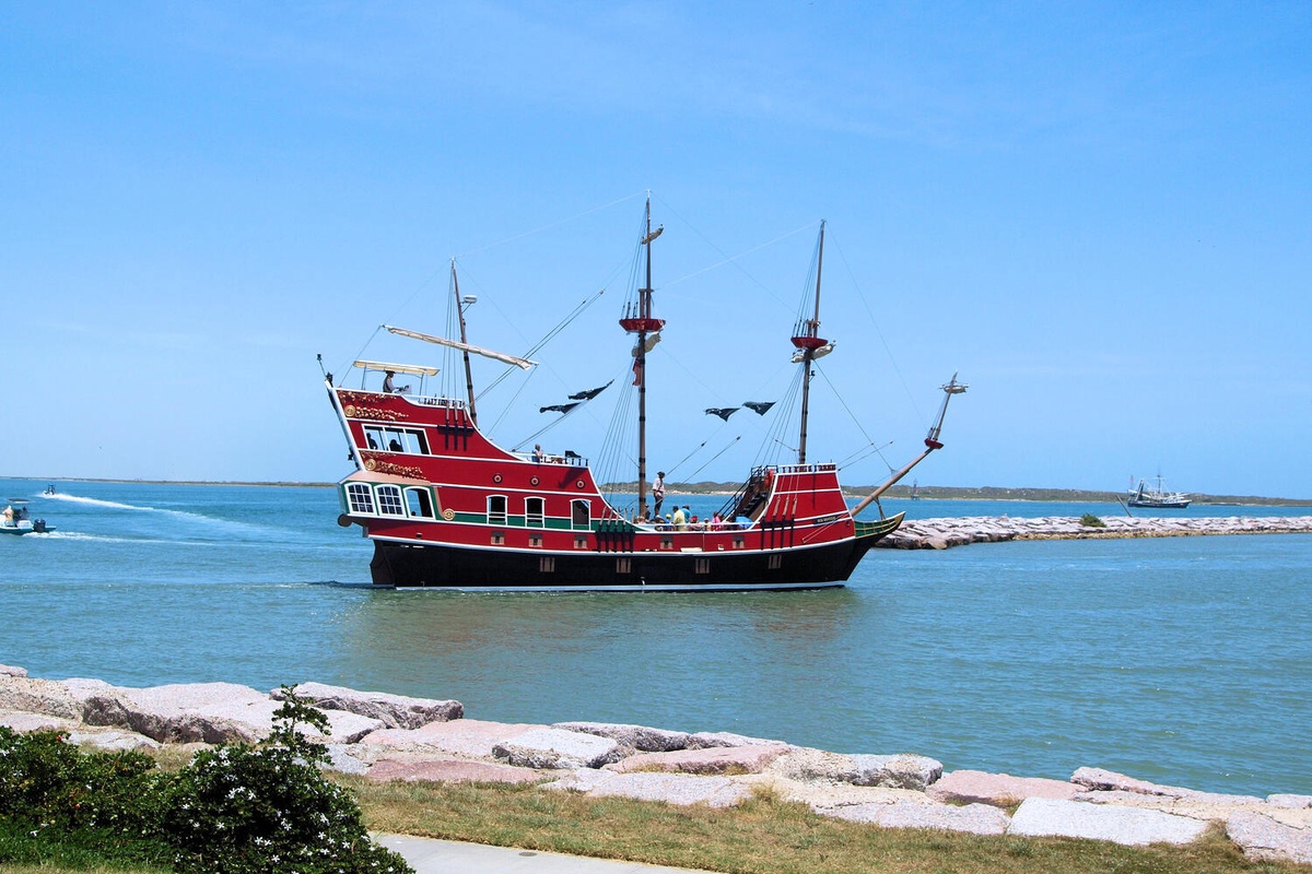 A classic red pirate ship anchors in crystal-clear waters near rocky shores, creating a picturesque maritime scene in the surrounding area.