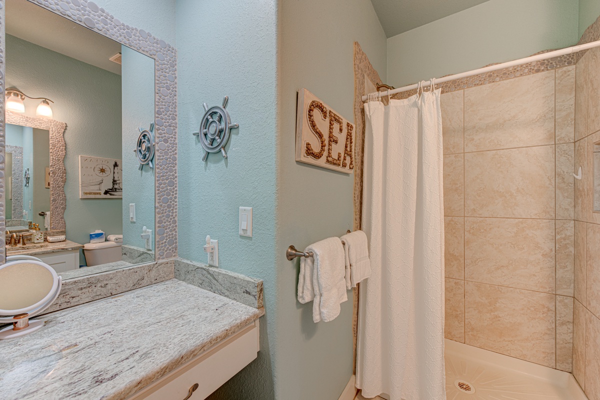 Your coastal-themed bathroom awaits with nautical charm, featuring a spacious tiled shower and fresh towels for your comfort.