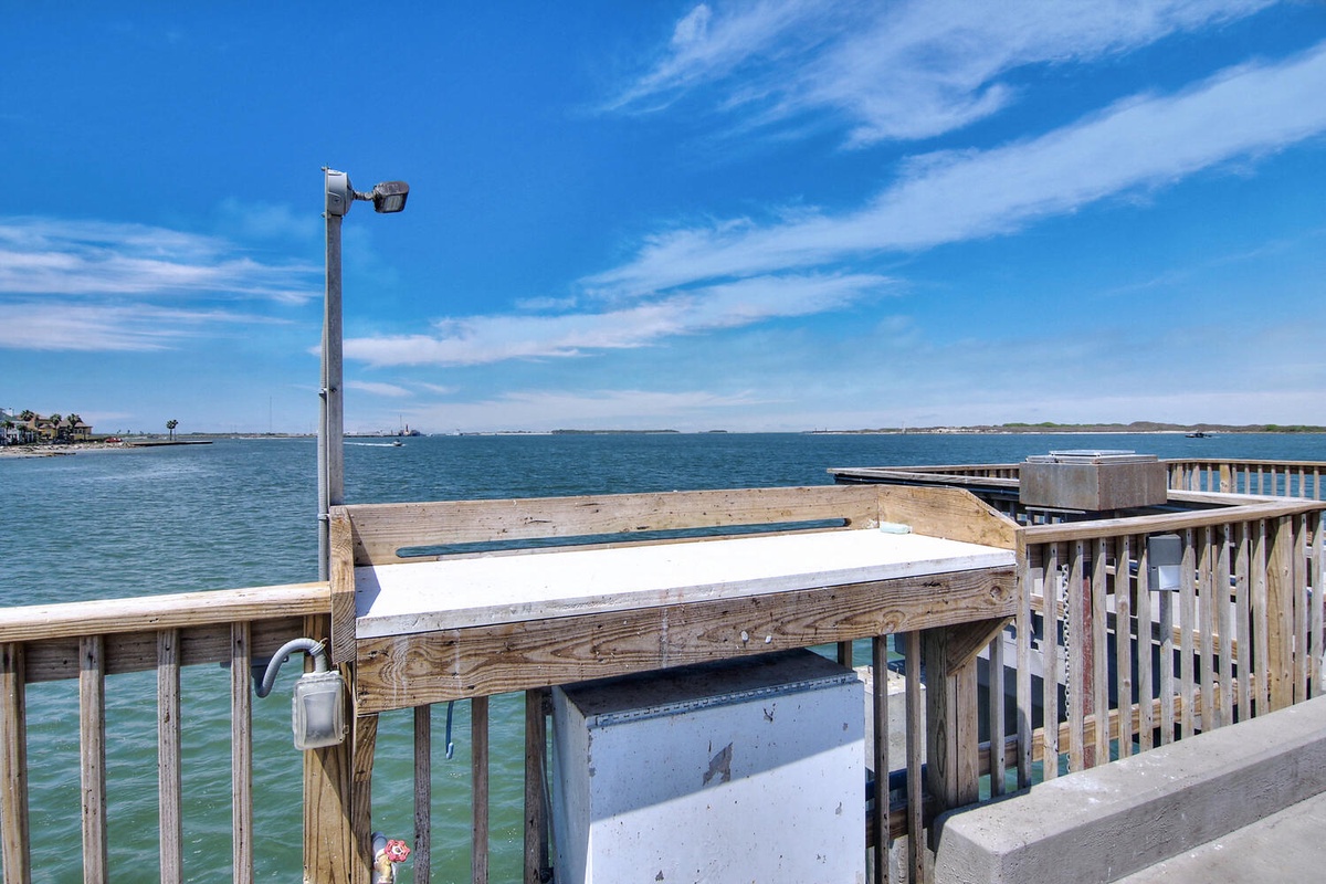 Waterfront pier with fish cleaning station overlooking calm blue waters and distant coastline.