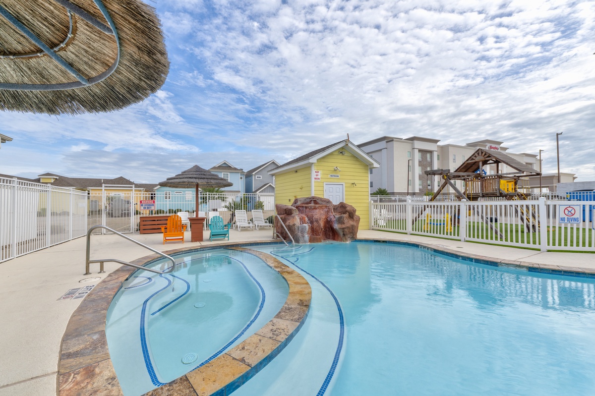 Swimming pool surrounded by colorful beach houses and outdoor seating in a coastal community setting.