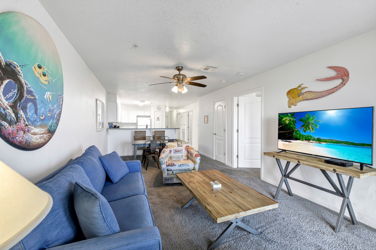 Relax in your ocean-themed living space with whimsical sea turtle murals, plush blue seating, and a large TV for movie nights.