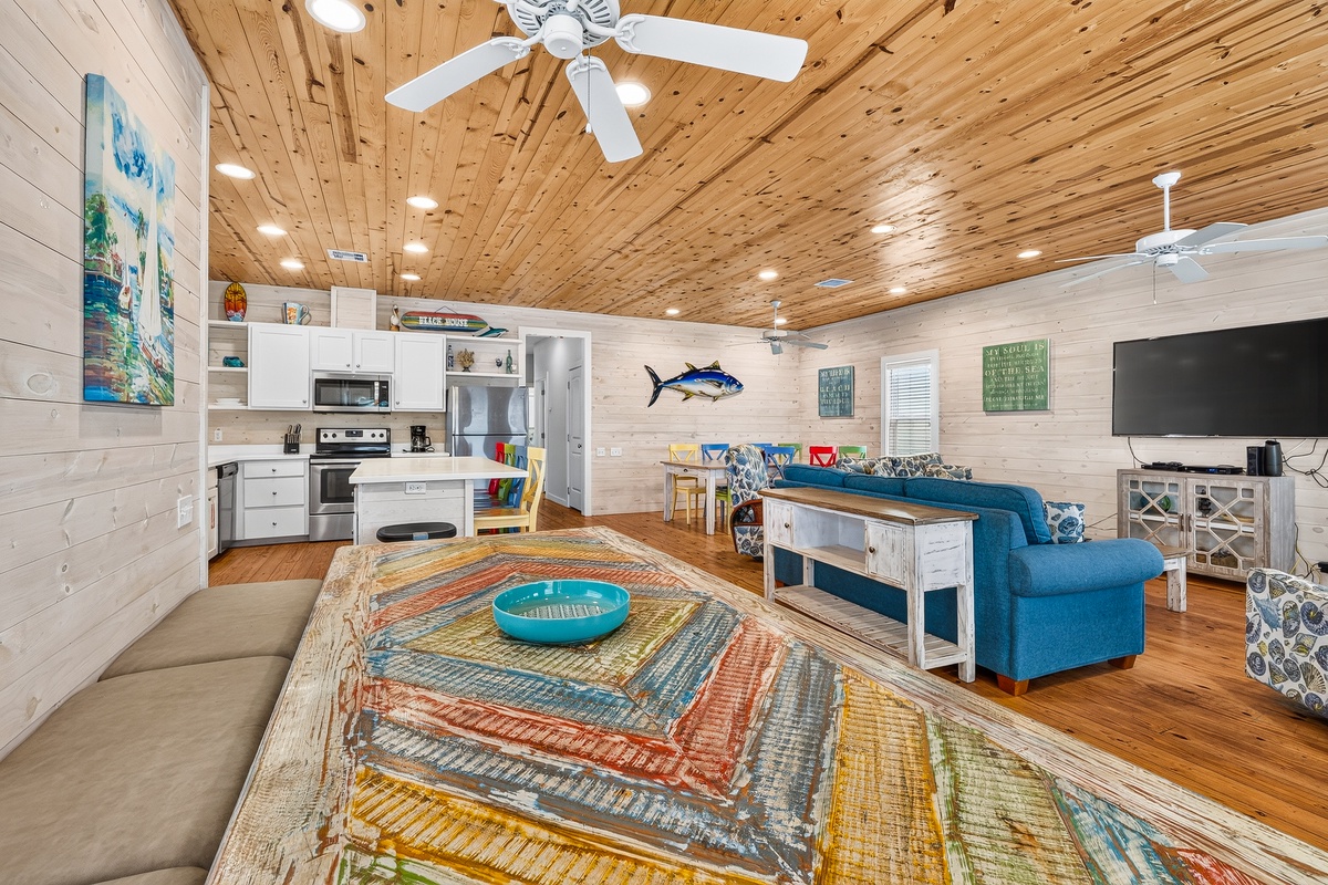 Step into your coastal retreat with warm wood ceilings and a bright open layout. The kitchen, living area, and dining space flow together seamlessly, inviting you to relax on the comfy blue sofa or gather around the table with loved ones.
