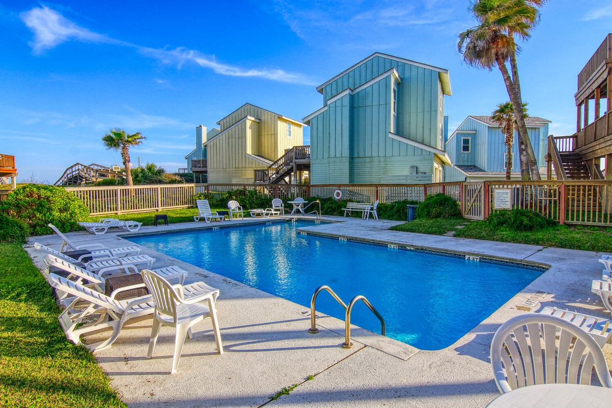 Sparkling community pool surrounded by colorful beach houses and swaying palms creates the perfect coastal retreat setting.