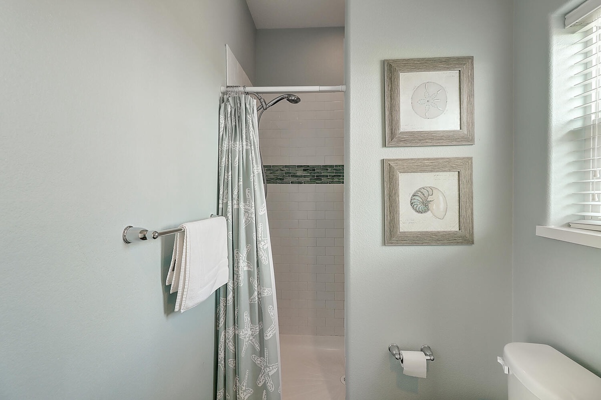 Step into your serene bathroom retreat with coastal artwork and refreshing shower ready for your relaxing getaway.