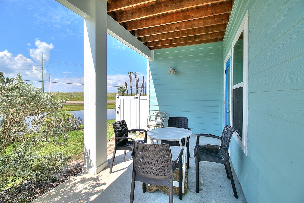 Your covered patio invites relaxing meals with water views, featuring a dining table surrounded by comfortable chairs under exposed wooden beams.