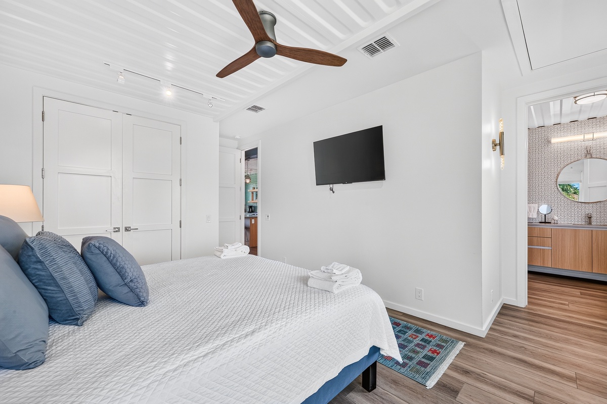 Drift off in your spacious primary retreat, where crisp white linens and soft coastal blues invite peaceful rest beneath a gently turning ceiling fan.