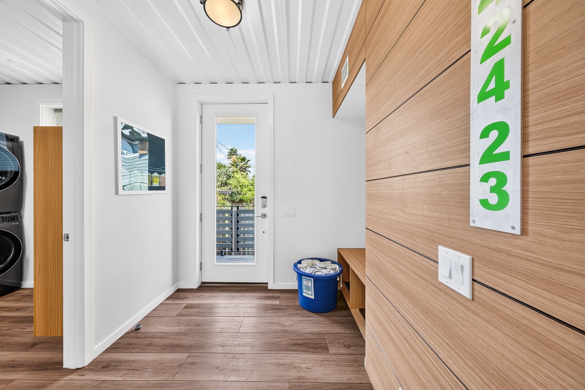 The entrance welcomes guests with sleek wood paneling, bright natural light through the glass door, and convenient storage space for your belongings.
