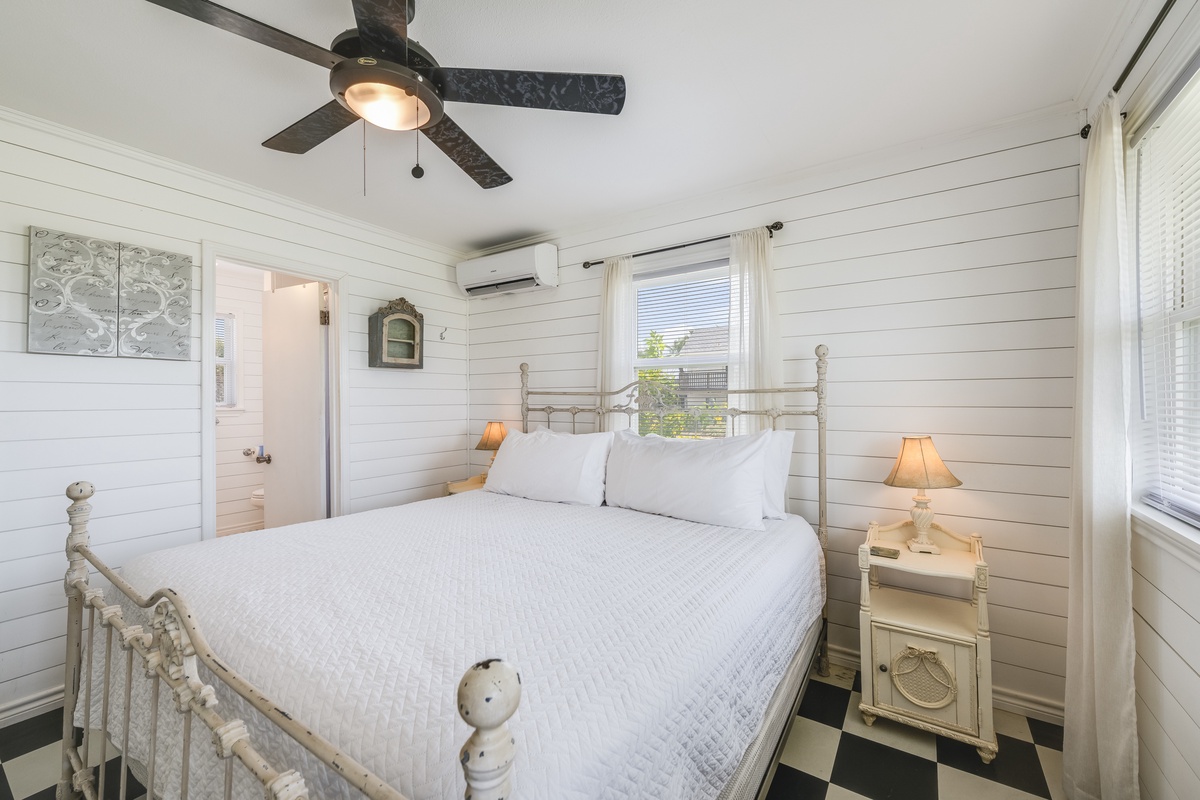 Your tranquil retreat awaits with crisp white linens, coastal charm, and gentle breezes from the ceiling fan above—perfect for peaceful mornings and restful nights.