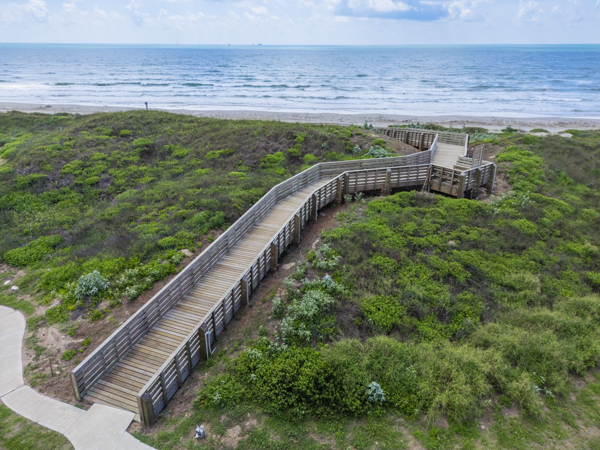 Wooden boardwalk winds through coastal dunes to pristine beach, offering scenic ocean access near the property.