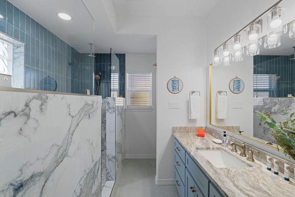Your luxurious spa-like bathroom features stunning marble finishes, elegant blue cabinetry, and a beautiful glass chandelier creating your perfect retreat.
