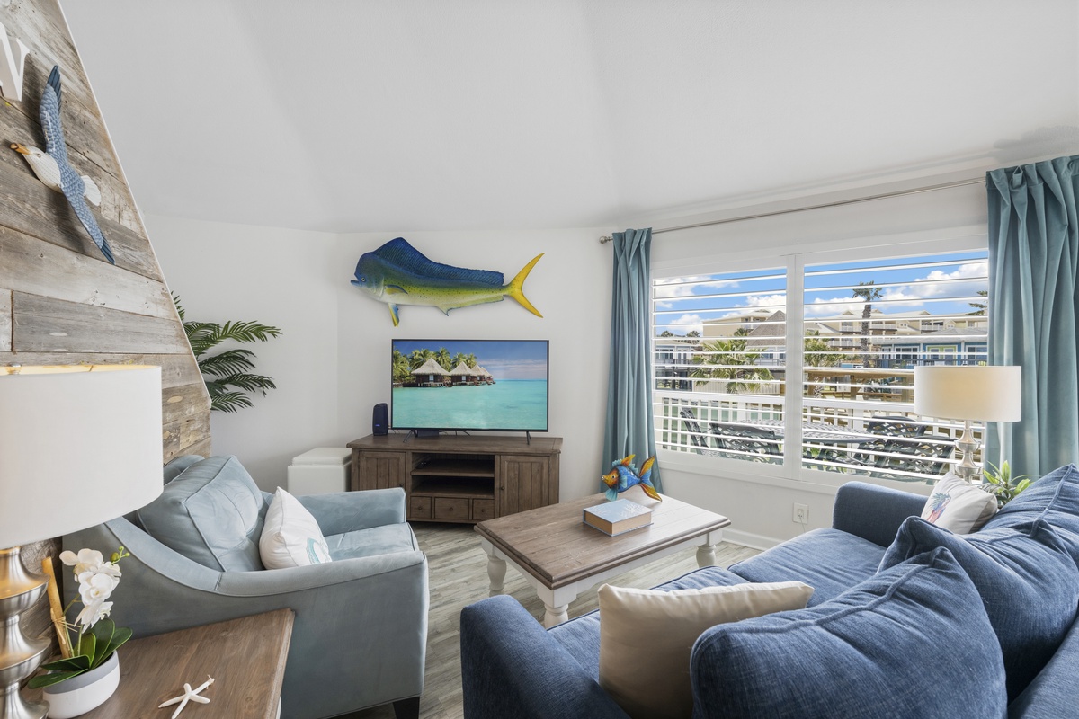 Relax in your coastal-themed living room featuring ocean blues, nautical decor, and large windows showcasing tropical views.