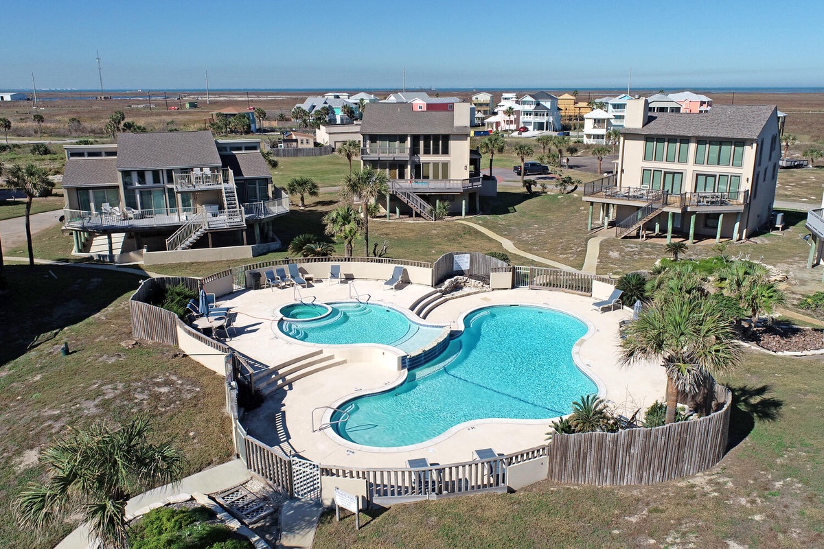 Aerial view of beachfront vacation rental community featuring a stunning multi-level swimming pool and hot tub area surrounded by coastal homes.