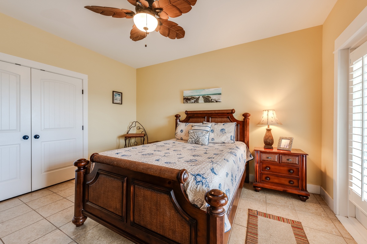 Unwind in your tropical-themed bedroom featuring elegant dark wood furniture, coastal décor, and a charming leaf-blade ceiling fan for perfect comfort.