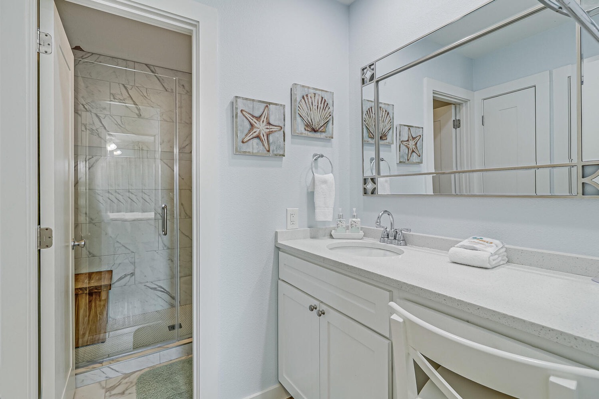 Your pristine bathroom features spa-like marble finishes, plush towels, and charming coastal artwork that creates a serene sanctuary for your morning routine.