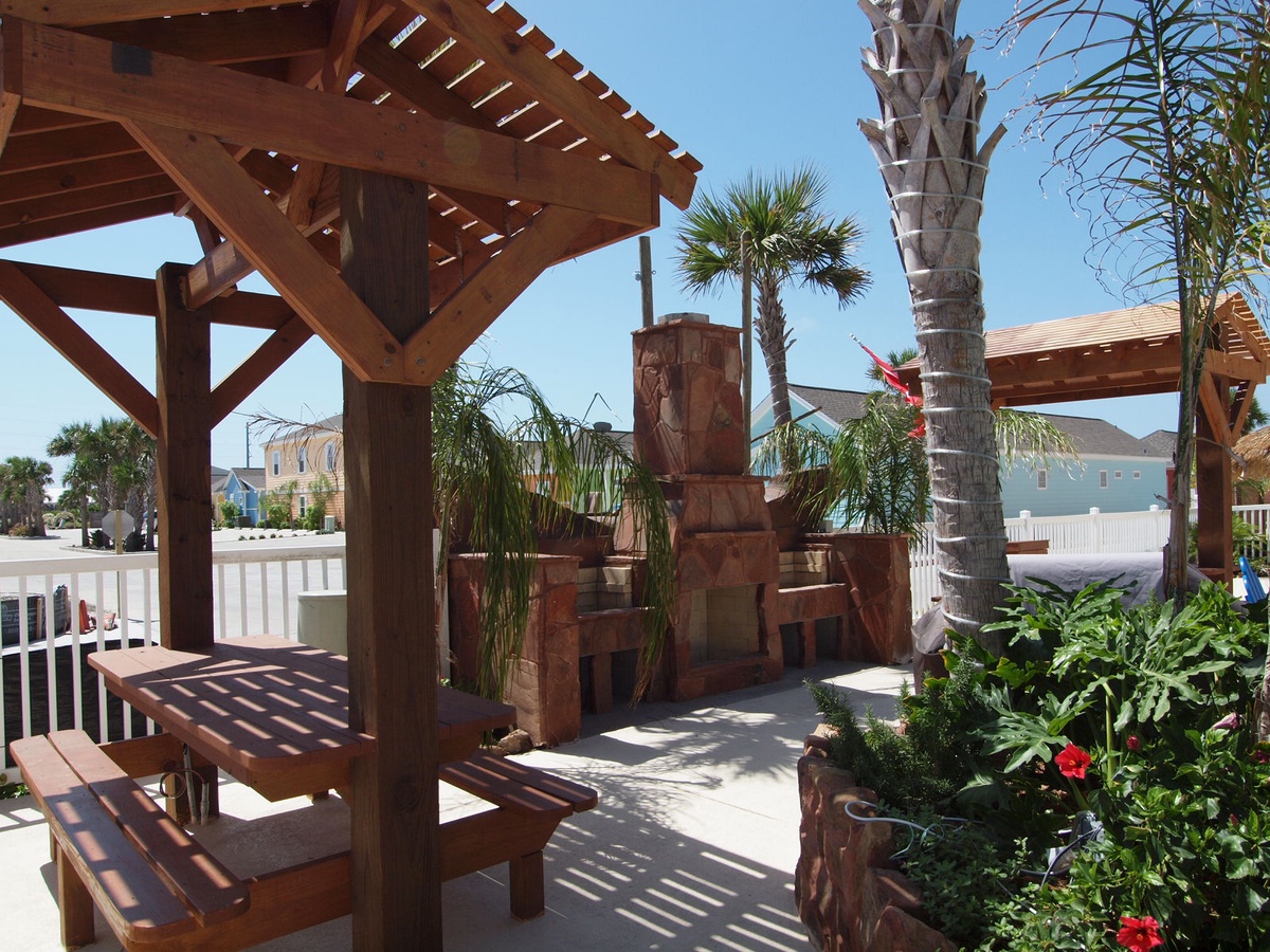 Relax under your private pergola with outdoor dining and stone fireplace, surrounded by tropical palms and flowering plants.