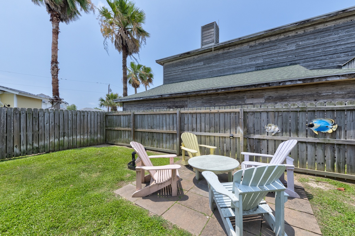 Your private backyard retreat features Adirondack seating around a fire pit table, perfect for evening conversations beneath swaying palms in this fenced outdoor space.
