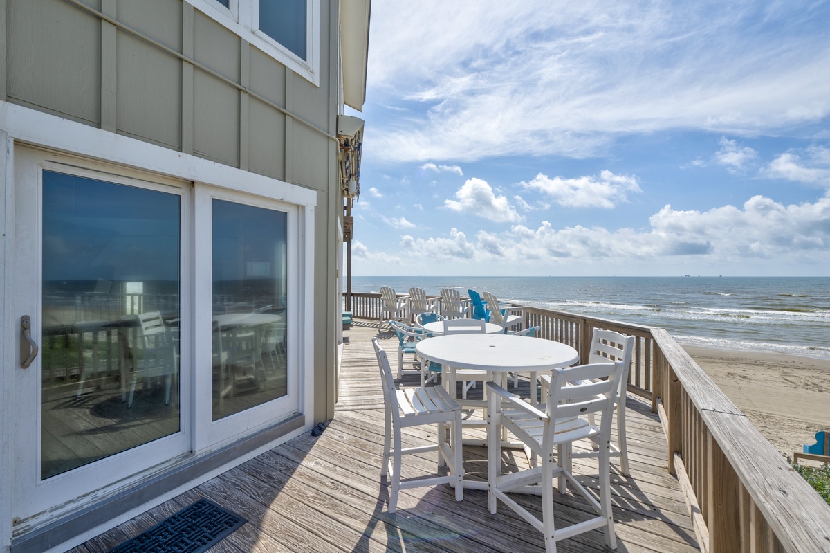This beachfront property features an expansive wooden deck with direct beach access, offering panoramic ocean views and coastal scenery perfect for outdoor gatherings.