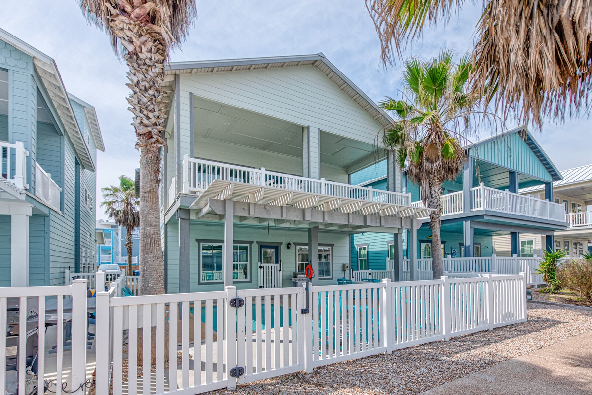 Coastal beach house featuring charming turquoise siding, wraparound porches, and tropical palm trees in a relaxed seaside neighborhood.