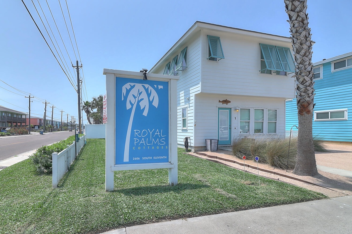 Royal Palms Cottages entrance welcomes visitors to a charming beachside community with colorful vacation homes and tropical palm trees.