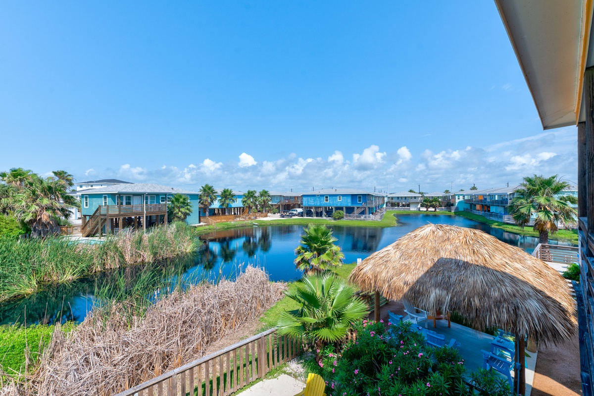 Tropical canal community with blue homes, palm trees, and thatched tiki huts creating a resort-like neighborhood atmosphere.