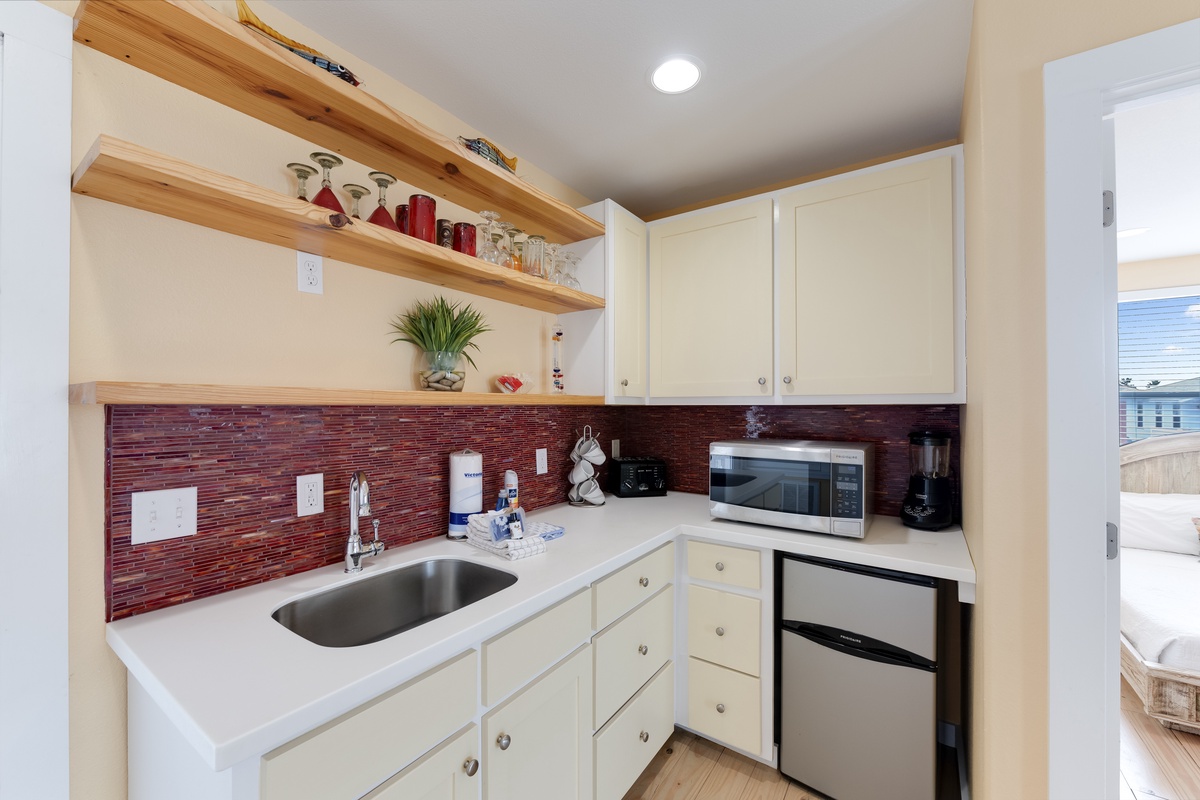 Your fully equipped kitchenette features white cabinets, sleek countertops, and a charming red brick backsplash—perfect for preparing your favorite meals.