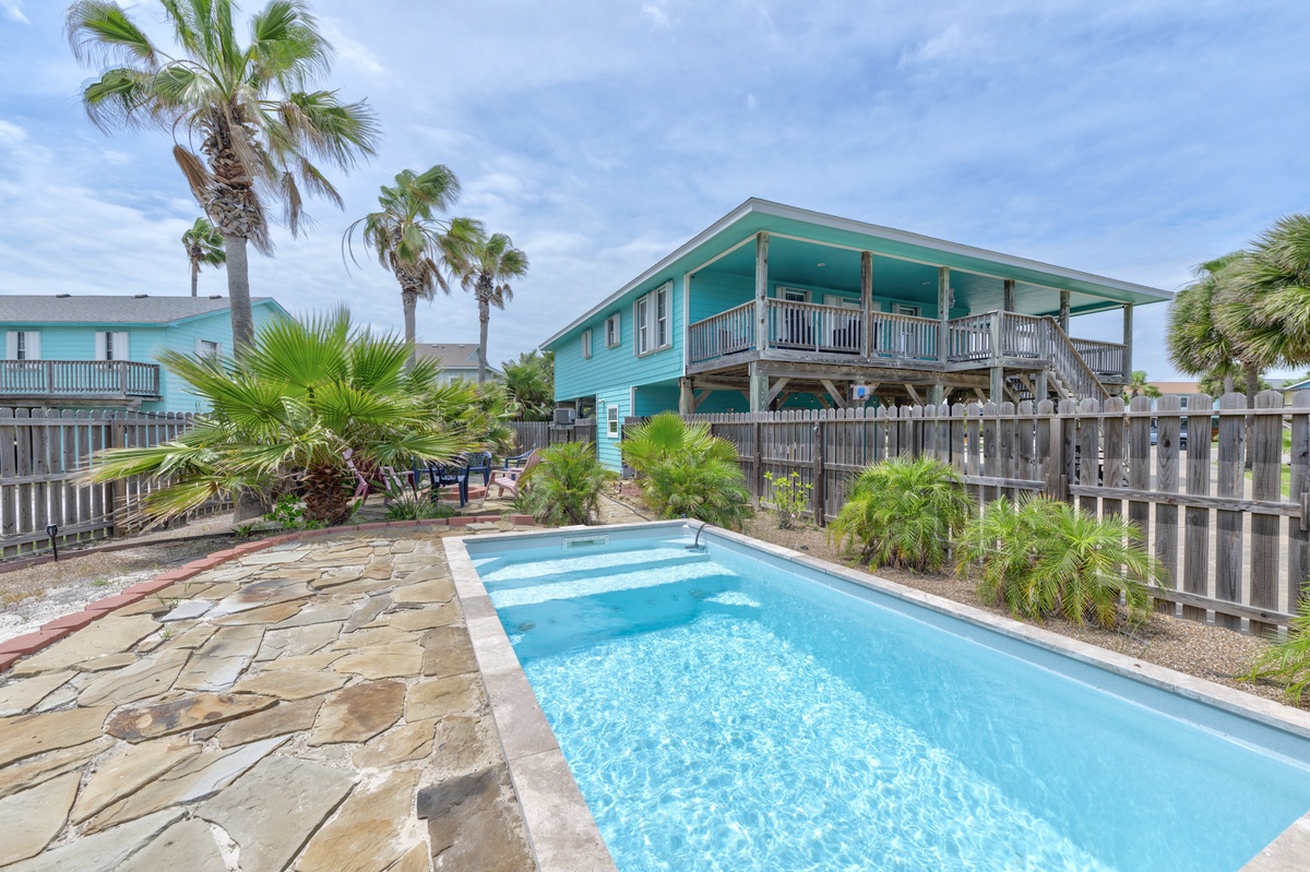 A coastal retreat featuring a private turquoise pool surrounded by tropical palms and natural stone patio. The elevated property showcases covered deck space perfect for outdoor relaxation.