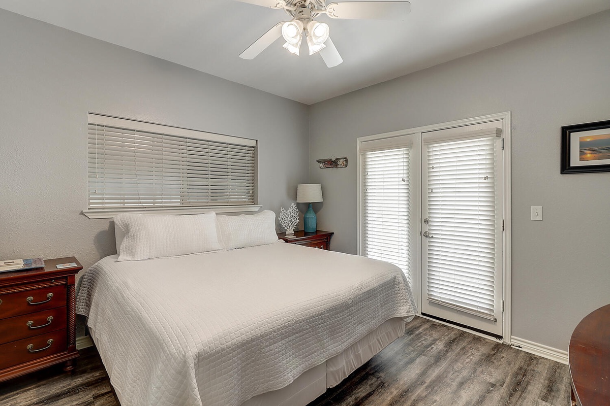 Sink into crisp white linens in your peaceful bedroom, where soft natural light filters through blinds and French doors lead to your private outdoor space.
