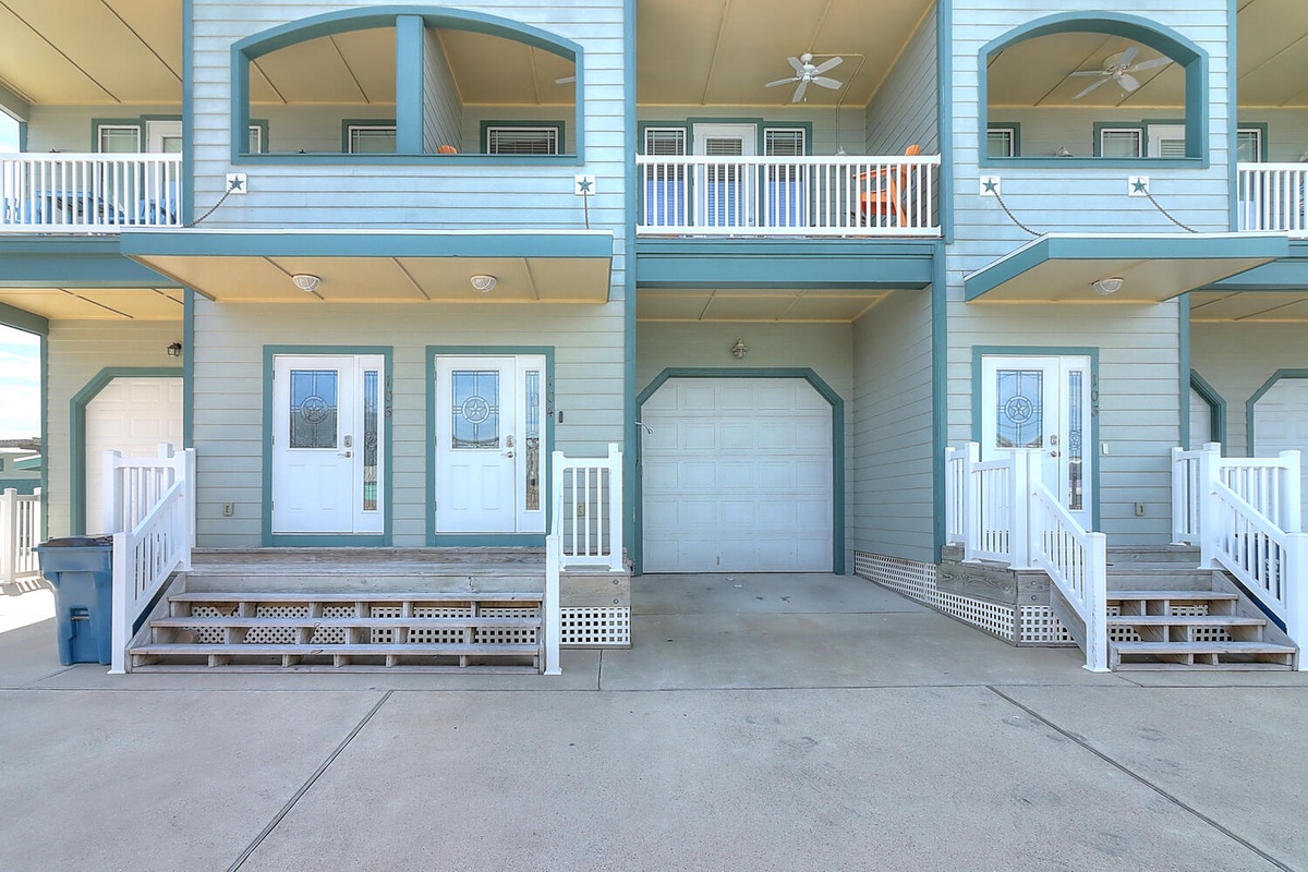 Coastal-style building exterior with covered parking and multiple unit entrances featuring white railings and blue trim.