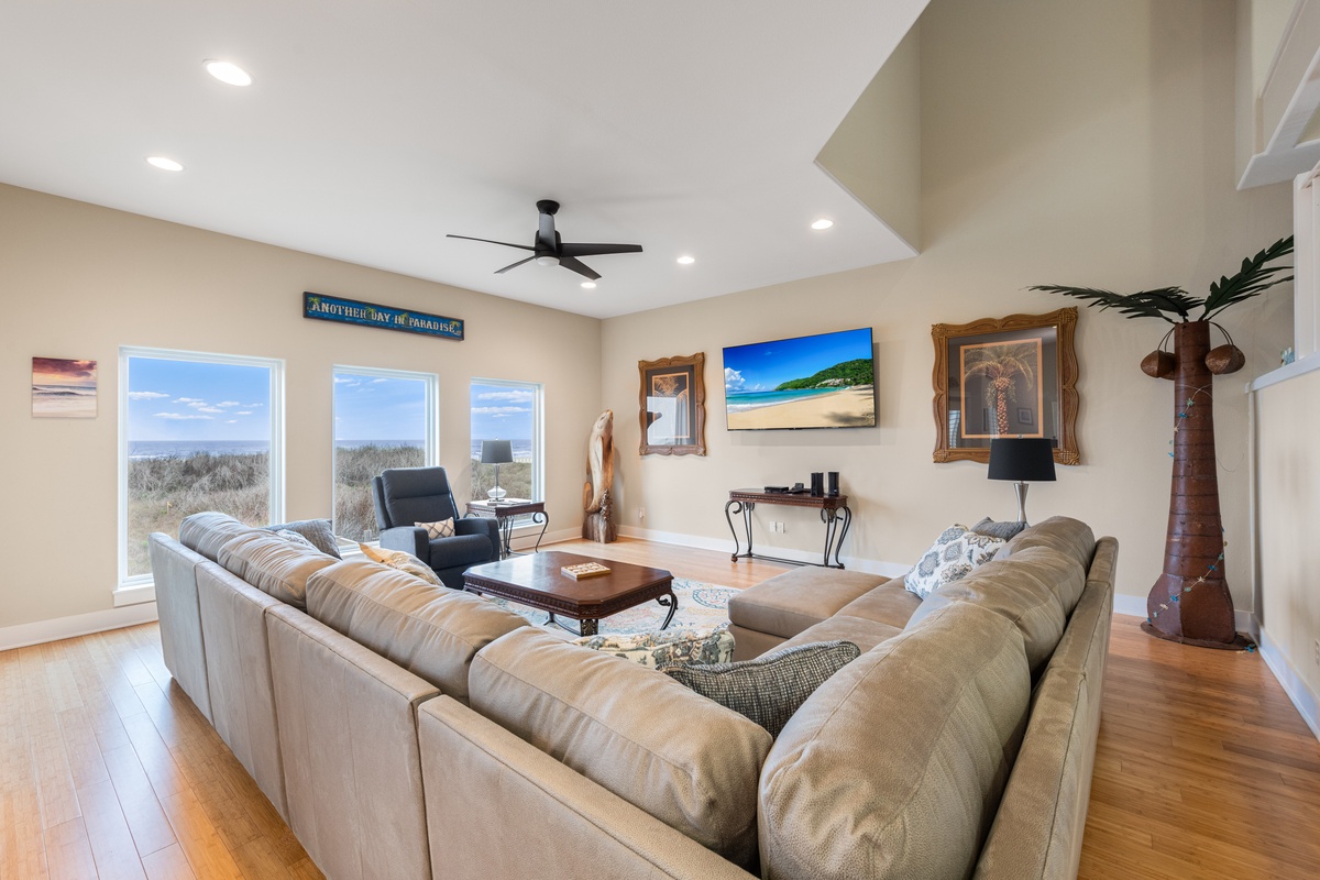Unwind in your spacious living room with plush sectional seating, coastal artwork, and stunning views of natural dunes through large windows.