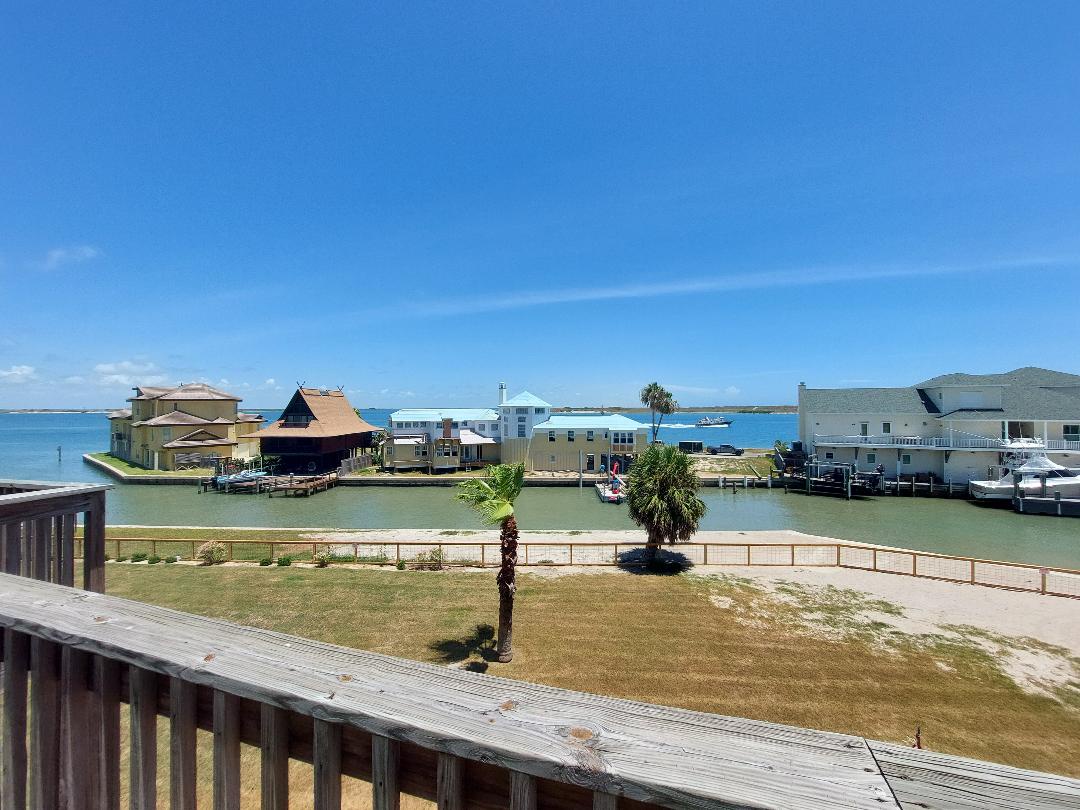 Waterfront community with colorful houses, boats, and palm trees under a bright blue sky.