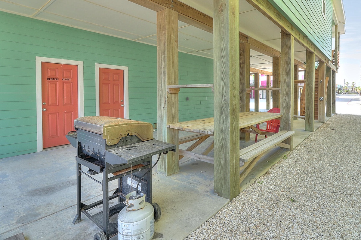 Colorful beach house exterior with covered porch seating and BBQ grill for convenient outdoor dining.