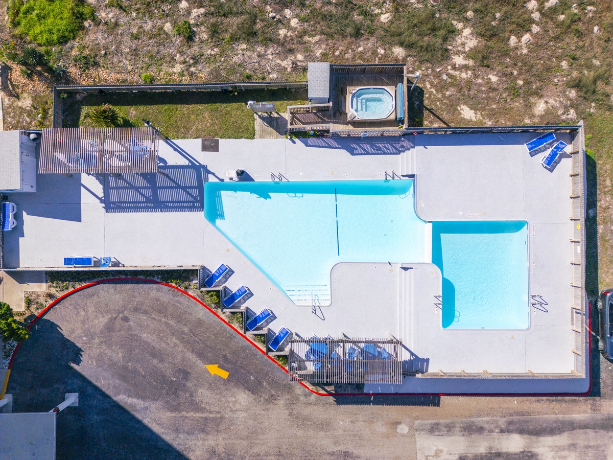 Aerial view of the property showcasing a large L-shaped swimming pool with surrounding deck area and multiple buildings.