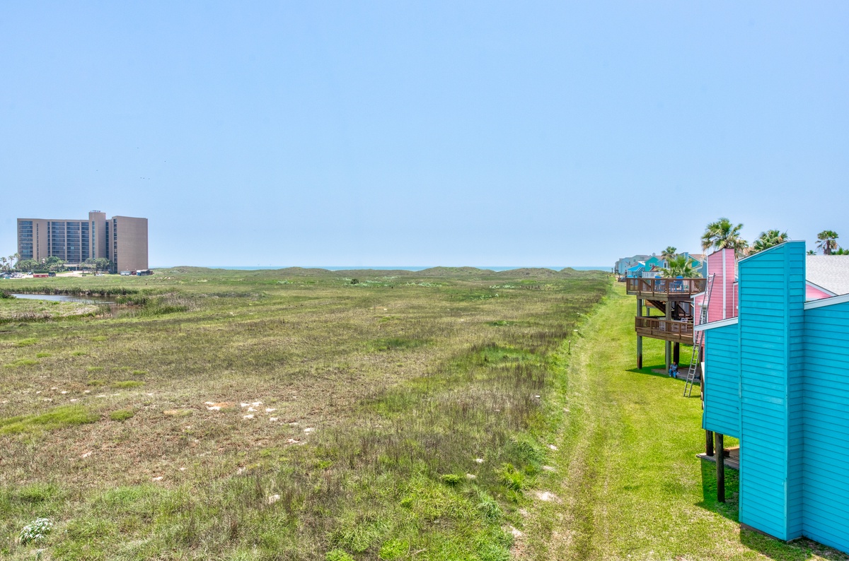 Colorful beachfront cottages on stilts overlook natural coastal dunes with distant skyline views creating a unique beach town setting.