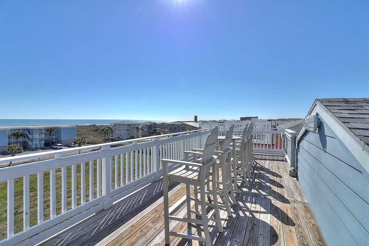 Expansive deck with ocean views and coastal neighborhood backdrop under clear blue skies.