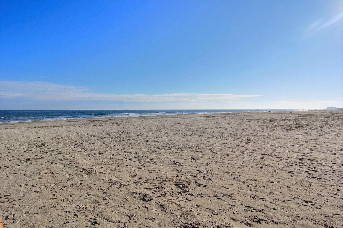 Expansive sandy beach stretches along the coastline with gentle waves and clear blue skies overhead.
